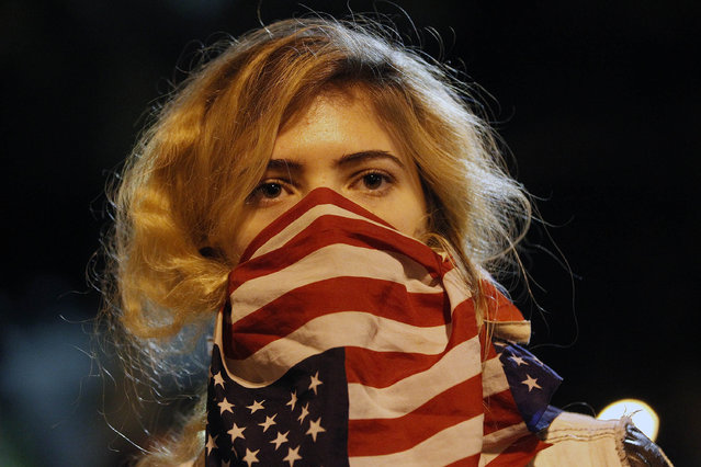 A woman wears a U.S. flag in front of her face during a rally near the Los Angeles Police Department headquarters in downtown Los Angeles on Tuesday, November 25, 2014. People protesting the Ferguson Mo., grand jury decision took to the streets in cities across the U.S. for the second day. (Photo by Nick Ut/AP Photo)