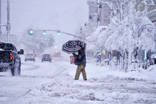 A passer-by uses an umbrella while crossing a snow-covered street, Tuesday, March 14, 2023, in Pittsfield, Mass. The New England states and parts of New York are bracing for a winter storm due to last into Wednesday. (Photo by Ben Garver/The Berkshire Eagle via AP Photo)