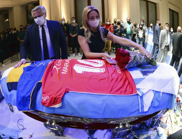 In this handout photo released by Argentina's Presidency, President Alberto Fernandez touches the coffin that contain the remains of Diego Maradona, while first lady Fabiola Yañez places a bouquet of roses on the casket adorned with his team jerseys, as they pay their final respects to Maradona, inside the presidential palace in Buenos Aires, Argentina, Thursday, November 26, 2020. (Photo by Argentina's Presidency via AP Photo)