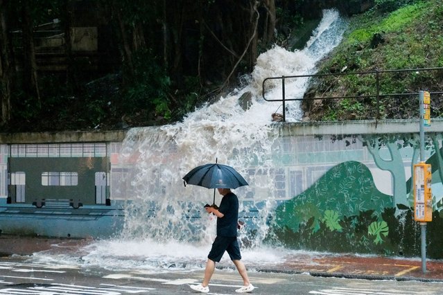 A pedestrian walks past an overflowing hillside drain spilling water onto a street in the Quarry Bay area of Hong Kong on August 5, 2025, amid a black rainstorm warning issued by the city's weather observatory. Parts of Hong Kong were brought to a standstill by flooding caused by heavy rains on August 5, after the highest-tier rainstorm warning was issued for the fourth time in eight days. (Photo by Tommy Wang/AFP Photo)