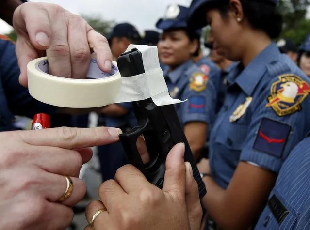 A police officer covers the muzzle of a service pistol of a policewoman with tape during a sealing of firearms ceremony at the National Capital Region Police Office in Taguig, Metro Manila, December 22, 2014. (Photo by Erik De Castro/Reuters)