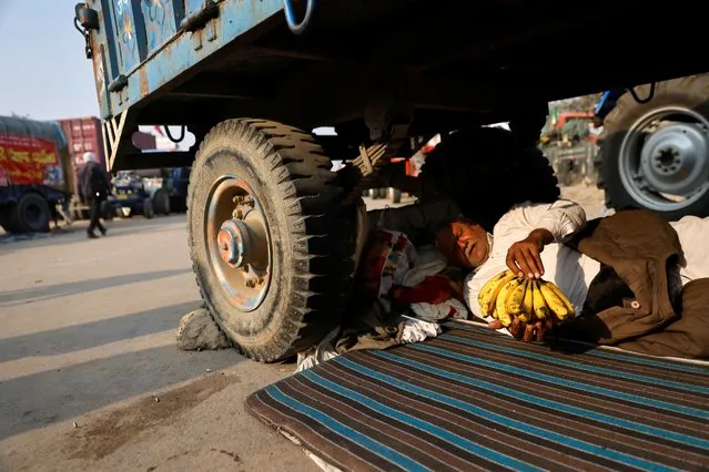 A farmer rests under a tractor trolley at a site of a protest against the newly passed farm bills at Singhu border near Delhi, India, November 30, 2020. (Photo by Danish Siddiqui/Reuters)