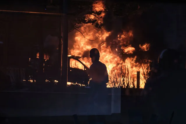 A passing bystander is reflected in a shop window as a South African police van is set on fire on October 25, 2016 in Johannesburg, during a university students' protest against tuition fees, racism and inequality. Weeks of demonstrations at South African universities have targeted high student tuition fees – but protestors say they are also about inequality in a society still plagued by the legacy of apartheid. (Photo by Gianluigi Guercia/AFP Photo)