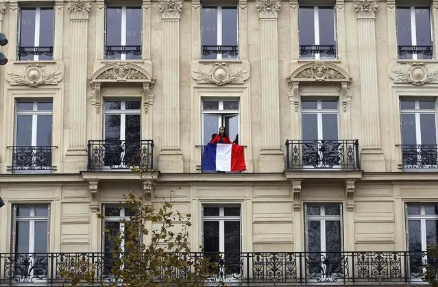 A woman stands on a balcony behind a French flag at an apartment building in the Place de la Republique in Paris, France, November 27, 2015 as the French President called on all French citizens to hang the tricolour national flag from their windows on Friday to pay tribute to the victims of the Paris attacks during a national day of homage. (Photo by Eric Gaillard/Reuters)