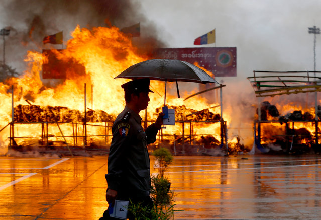 Myanmar police officer walks past near a pile of illegal drugs burning during a “Destruction Ceremony of Seized Narcotic Drugs”, held to mark the International Day against Drug Abuse in Yangon, Myanmar, 26 June 2018. Myanmar authorities destroyed an assortment of drugs worth some 184.98 million US dollar in Yangon, Mandalay and Taunggyi. (Photo by Nyein Chan Naing/EPA/EFE)