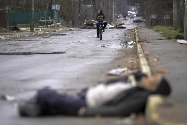A man and child on a bicycle come across the body of a civilian lying on a street in the formerly Russian-occupied Kyiv suburb of Bucha, Ukraine, Saturday, April 2, 2022. (Photo by Vadim Ghirda/AP Photo)