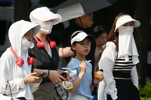 People wear head coverings during a heatwave in Beijing on June 23, 2023. (Photo by Greg Baker/AFP Photo)