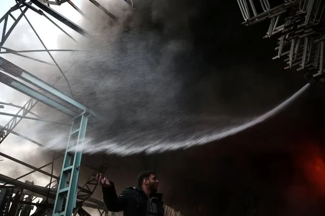 A member of the Syrian Civil Defense, known as the White Helmets, guides a colleague to extinguish fire following a reported government airstrike on the rebel-held town of Douma, on the eastern outskirts of the capital Damascus, on November 17, 2016. Douma, the largest town in the Eastern Ghouta area with more than 100,000 residents, is surrounded and regularly shelled by regime forces. (Photo by Sameer Al-Doumy/AFP Photo)