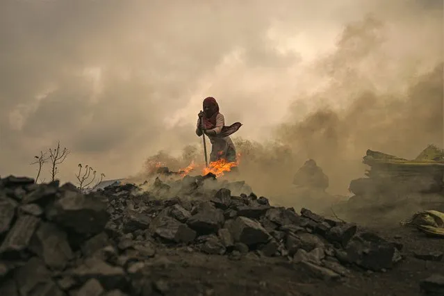 A girl burns raw coal to make it usable for further sale near an open cast mining site on the outskirts of Dhanbad on July 6, 2023. (Photo by Money Sharma/AFP Photo)