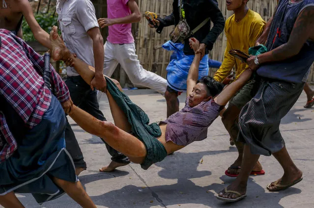 Anti-coup protesters carry an injured man after a clash with riot policemen and soldiers in Yangon, Myanmar Sunday, March 14, 2021. (Photo by AP Photo/Stringer)