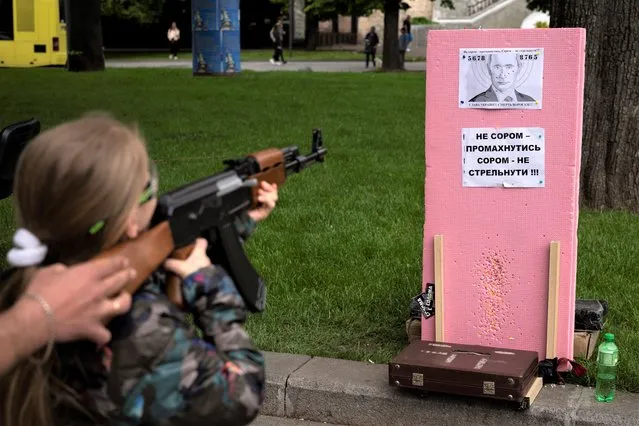 Victoria, 7, uses a plastic Kalashnikov rifle to shoot balls at a portrait of Russian President Vladimir Putin, at a street attraction in the centre of Lviv, Ukraine on Saturday, May 14, 2022. The banner reads in Ukrainian: It's not a shame to miss. It's a shame not to try to shoot! Glory to Ukraine, Death to our enemies!. (Photo by Emilio Morenatti/AP Photo)