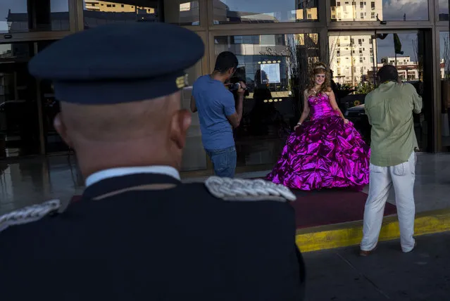 In this December 13, 2015 photo, Amanda Teresa Betancourt, who lives in Cuba, poses during a quinceanera photo session as a hotel doorman stands by in Havana, Cuba. Cuban reforms permitting small-scale, private businesses and the re-establishment of U.S.-Cuban diplomatic relations have encouraged new photo and event planning businesses for events such as girls' 15th birthdays. (Photo by Ramon Espinosa/AP Photo)