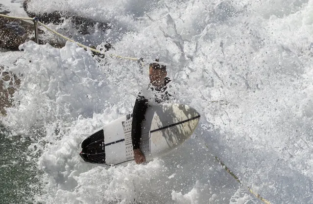 A surfer is enveloped by a wave as he waits to jump off the rocks at Bronte Beach as large waves hit the Sydney coastline Monday, April 12, 2021. (Photo by Mark Baker/AP Photo)