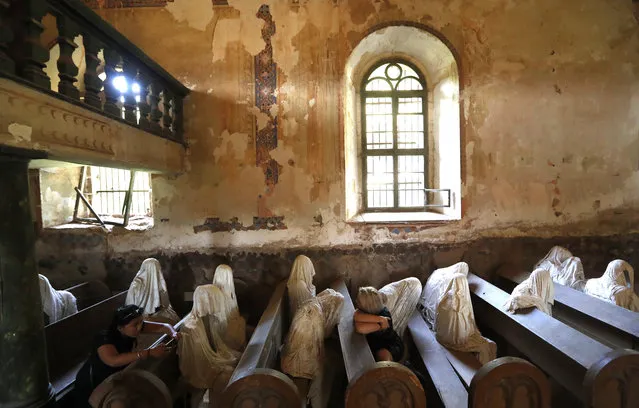 In this picture taken on Thursday, August 30, 2018, French tourists visit the church of Saint George in the village of Lukova, Czech Republic. In the year of 2012 the art student Jakub Hadrava filled the church's pews with ghostly figures, made from plaster casts of live models draped in white cloth. The effect is chilling. He called the work “My Mind”. (Photo by Petr David Josek/AP Photo)