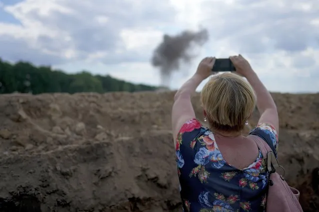 A journalist takes a picture of smoke rising from a landmine exploded by a Ukrainian specialized team working on a field to clean the area on the outskirts of Kyiv, Ukraine, Thursday, June 9, 2022. (Photo by Natacha Pisarenko/AP Photo)