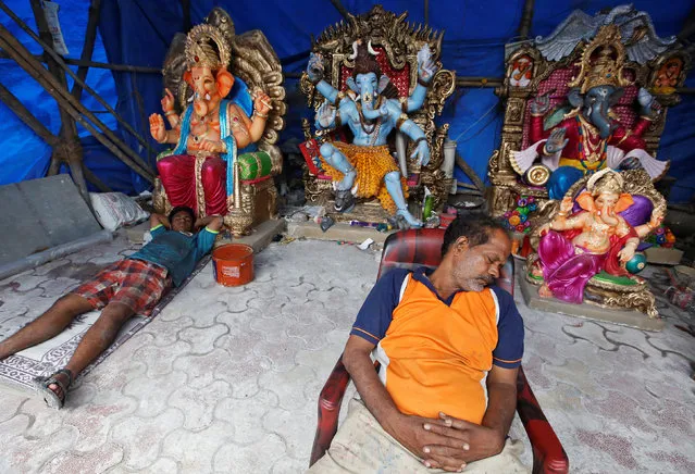 Workers sleep beside the idols of Hindu god Ganesh, the deity of prosperity, on the first day of the ten-day-long Ganesh Chaturthi festival, inside a workshop in Mumbai, India, September 13, 2018. (Photo by Francis Mascarenhas/Reuters)