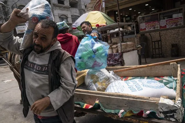 A bag of foodstuffs provided by the United Nations Relief and Works Agency for Palestine Refugees in the Near East (UNRWA) sits on the back of a pull cart as Palestinians collect food aid following a cease-fire reached after an 11-day war between Gaza's Hamas rulers and Israel, in Gaza City, Saturday, May 22, 2021. (Photo by John Minchillo/AP Photo)