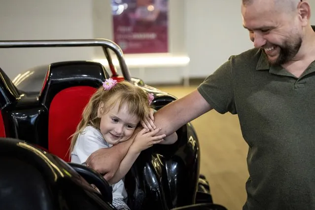 Four-year-old Daryna holds the arm of her father, Valentyn Lytvynchuk during an outing in Lviv, Ukraine, July 20, 2023. He is a former battalion commander of the 5th brigade and lost his leg in fighting. Daryna painted a unicorn on his prosthetic. Ukraine is facing the prospect of a future with upwards of 20,000 amputees, many of them soldiers who are also suffering psychological trauma from their time at the front. (Photo by Evgeniy Maloletka/AP Photo)