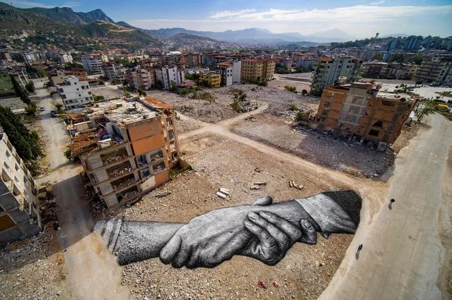 This aerial photograph taken on October 5, 2023 in Antakya and released by Saype, shows a giant biodegradable landart painting located between damaged buildings by French-Swiss artist Guillaume Legros, known as Saype, from the Beyond Walls project in Hatay. The black-and-white fresco – two hands intertwined, his trademark – covers 1,000 m2, where until the night of February 6, 2023 stood four- to five-storey buildings with first floors occupied by a pastry shop, a tailor or a glazier. (Photo by LeSabe/Handout via AFP Photo)