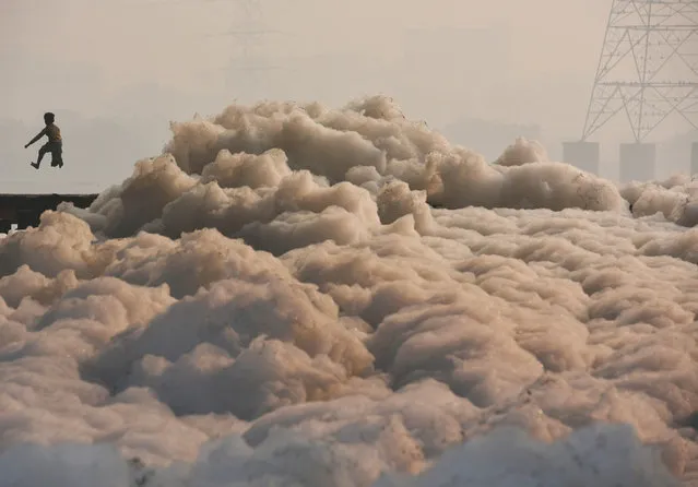 A boy runs over a bridge along a large amount of toxic industrial waste-foam formed along the banks of polluted Yamuna River, on December 2, 2018 in New Delhi, India. (Photo by Biplov Bhuyan/Hindustan Times via Getty Images)