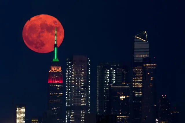 The full moon rises behind the Empire State Building in New York City, New York, U.S., July 23, 2021. (Photo by Bjoern Kils/New York Media Boat via Reuters)