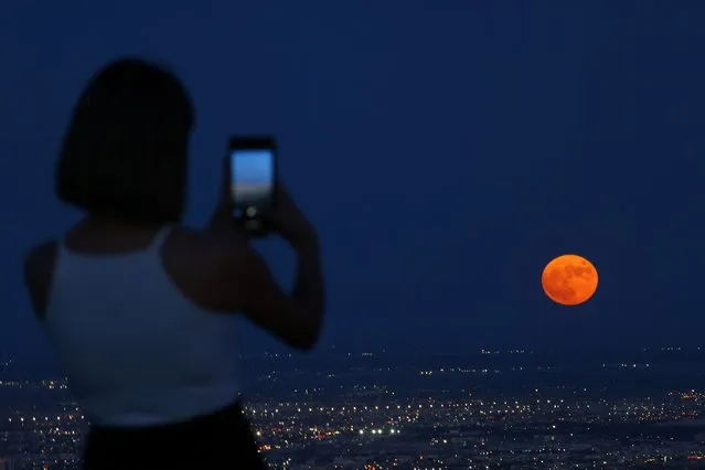 A woman takes a picture as a super moon, known as the Blue Moon, rises above Ciudad Juarez, Mexico on August 30, 2023. (Photo by Jose Luis Gonzalez/Reuters)
