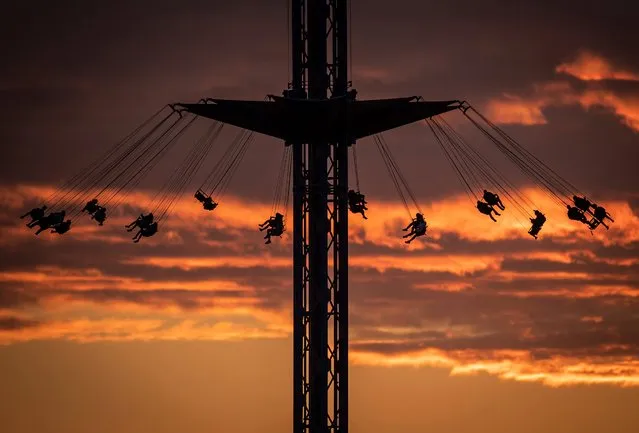 People are silhouetted while riding the Atmosfear double swing, which lifts riders more than 66 meters into the air while spinning at up to 70 km/h, at the Pacific National Exhibition at sunset in Vancouver, British Columbia, on Tuesday, August 31, 2021. (Photo by Darryl Dyck/The Canadian Press via AP Photo)