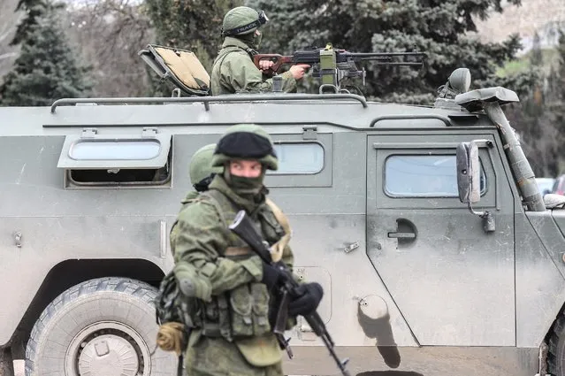Troops in unmarked uniforms stand guard in Balaklava on the outskirts of Sevastopol, Ukraine, Saturday, March 1, 2014. An emblem on one of the vehicles and their number plates identify them as belonging to the Russian military. (Photo by Andrew Lubimov/AP Photo)