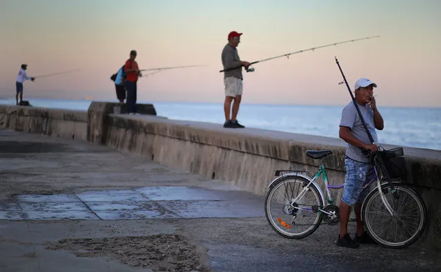 A man smokes a cigarette as people fish on the Malecon in Havana, Cuba, March 25, 2019. (Photo by Phil Noble/Reuters)