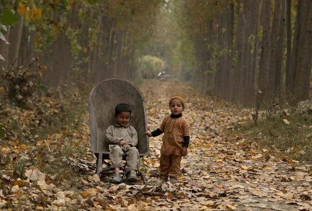 Children wait for their father working nearby, on the outskirts of Peshawar, Pakistan, Sunday, December 5, 2021. (Photo by Muhammad Sajjad/AP Photo)