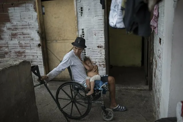 Giancarlo Paredes, better know as “El Mocho”, who uses a wheelchair after losing his leg in a shootout with police, holds his daughter in a squatter building in the Petare slum of Caracas, Venezuela, Monday, May 13, 2019. “I was jailed for 17 years, and I can tell you that crime is going down, because nowadays no one has money here in Venezuela and the bullets are in dollars”, said Paredes, who added that many of his criminal friends have immigrated to other countries. Paredes was in jail for robbery and kidnapping. (Photo by Rodrigo Abd/AP Photo)