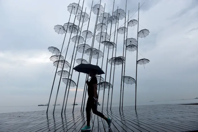 A woman with an umbrella walks under the rain past a sculpture called “Umbrellas” by Greek sculptor George Zongolopoulos along the waterfront in Thessaloniki on July 30, 2018. (Photo by Sakis Mitrolidis/AFP Photo)