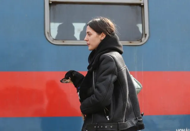 A woman fleeing Russia's invasion of Ukraine carries a dog as she gets on a train to Budapest departing from Zahony, Hungary on March 15, 2022. (Photo by Bernadett Szabo/Reuters)
