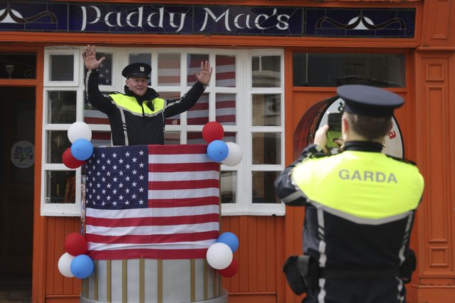 An Irish police officer poses for a colleague to take a photo as last minute preparation are made with bunting and US flags put up in the town of Ballina ahead of the visit by President Joe Biden to St Muredach's Cathedral, in Ballina, Ireland, Friday, April 14, 2023. The President will give a speech later Friday outside the cathedral. (Photo by Peter Morrison/AP Photo)