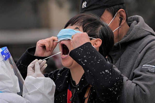 A woman pulls up her mask to get her throat swab at a coronavirus testing site near  residential buildings, Wednesday, April 6, 2022, in Beijing. (Photo by Andy Wong/AP Photo)