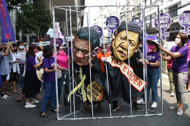 Women activists hold a makeshift prison cell with colleagues wearing masks depicting President Rodrigo Duterte (L) and Bongbong Marcos (R), son of the late dictator Ferdinand Marcos, and currently presidential aspirant for the May 9 elections, during a march to Malacanang Palace to celebrate International Women's Day in Manila on March 8, 2022. (Photo by Ted Aljibe/AFP Photo)