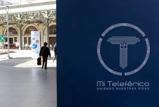 People walk past as the logo of the “Mi Teleferico” (My Cable Car) company is seen displayed at the Central station in La Paz, July 23, 2015. (Photo by David Mercado/Reuters)