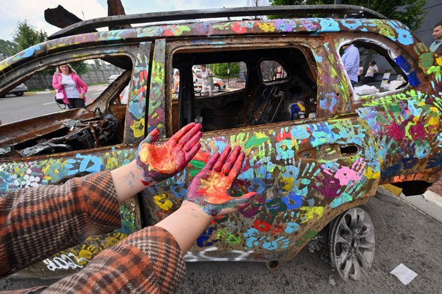 Ukrainian children decorate a burned car with colourful handprints for the local “Museum of Memory” during an art action in Bucha, north of Kyiv on June 30, 2023. (Photo by Sergei Supinsky/AFP Photo)