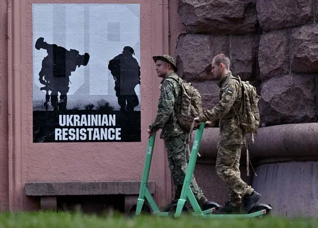 Ukrainian servicemen ride electric scooters past a placard reading “Ukrainian resistance” in the center of Kyiv on June 1, 2022 amid the Russian invasion of Ukraine. (Photo by Sergei Supinsky/AFP Photo)