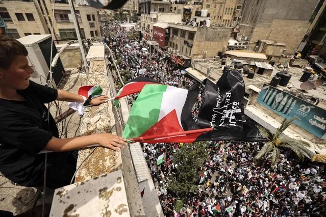A young Palestinian waves national flags from a rooftop as people march in a rally marking the 74th anniversary of the “Nakba“ or “catastrophe”, in the occupied West Bank town of Ramallah, on May 15, 2022. Each year Palestinians commemorate the “Nakba” on May 15, the official date of Israel's creation, as a result of which more than 760,000 Palestinians were pushed into exile or driven out of their homes. (Photo by Abbas Momani/AFP Photo)