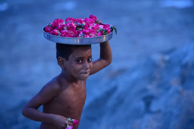 An Indian boy sells flowers to Hindu devotees of Lord Shiva as they perform rituals after collecting water from the river Ganges during the holy month of Shravan, In Allahabad on July 22, 2019. Shravan is considered the holiest month in the Hindu calendar with many religious festivals and ceremonies. (Photo by Sanjay Kanojia/AFP Photo)