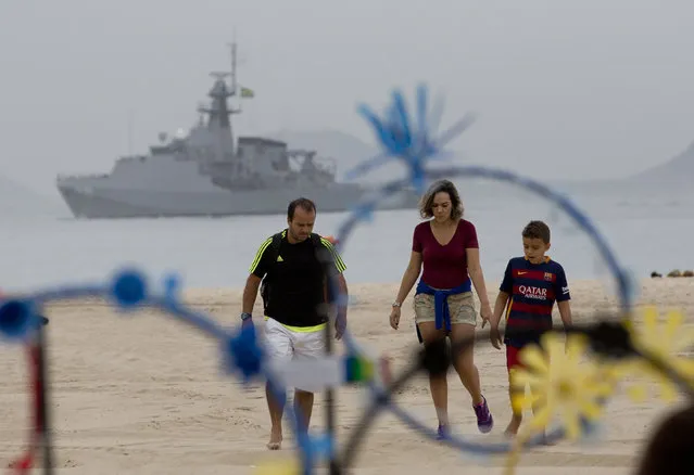 A family walks on the shore of Copacabana beach backdropped by a Brazilian navy vessel, in Rio de Janeiro, Brazil, Thursday, July 21, 2016. Brazilian police arrested 10 people who allegedly pledged allegiance to the Islamic State group on social media and discussed possible attacks during the Rio de Janeiro Olympics, officials said Thursday. (Photo by Silvia Izquierdo/AP Photo)