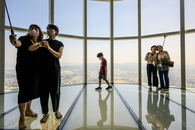 Visitors pose for selfies as a young boy walks on the observation deck at the Lotte World Tower Seoul Sky in Seoul on August 12, 2022. (Photo by Anthony Wallace/AFP Photo)