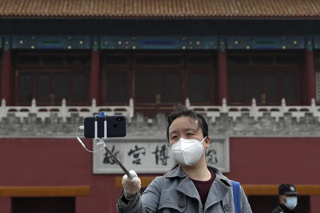 A woman wearing a protective face mask to help prevent the spread of the new coronavirus takes a selfie near the closed Forbidden City, usually crowded with tourists before the new coronavirus outbreak, in Beijing, Sunday, April 19, 2020. The pandemic that began in China in December is believed to have infected more than 2 million people worldwide. While most recover, at least over 150,000 have died, according to a tally by Johns Hopkins University based on figures supplied by health authorities around the globe. (Photo by Andy Wong/AP Photo)