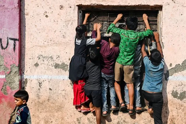 Children climb up onto the windows of a school building to catch a glimpse of a performance by artists dressed as cartoon characters inside the Dharavi slums in Mumbai on October 14, 2022. (Photo by Indranil Mukherjee/AFP Photo)