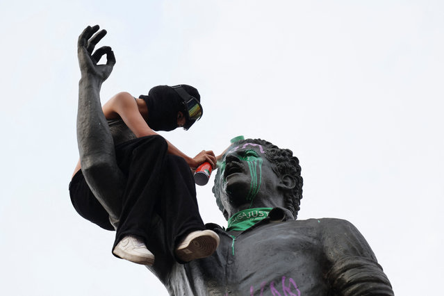 A woman sprays paint on the statue of Luis Carlos Galan during a protest to mark International Women's Day in Bogota, Colombia on March 8, 2025. (Photo by Luisa Gonzalez/Reuters)