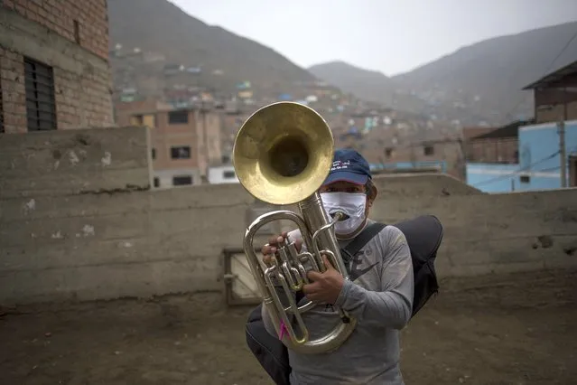 Musician Fernando Herrera plays a brass instrument as he and his band, “Santa Lucia”, who have lost their source of income due to restrictions amid the new coronavirus, perform for residents in hopes of monetary donations as they make their way through the Comas district of Lima, Peru, Friday, July 17, 2020. (Photo by odrigo Abd/AP Photo/)