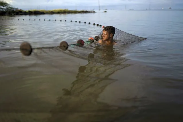 Enderson Mendoza cleans a fishing net as he and others fish for shrimp in Lake Maracaibo near Cabimas, Venezuela, Wednesday, October 12, 2022. (Photo by Ariana Cubillos/AP Photo)