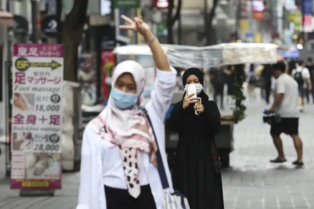 A woman wearing a face mask to help protect against the spread of the coronavirus takes photos of her friend at a shopping street in Seoul, South Korea, Wednesday, August 5, 2020. (Photo by Ahn Young-joon/AP Photo)