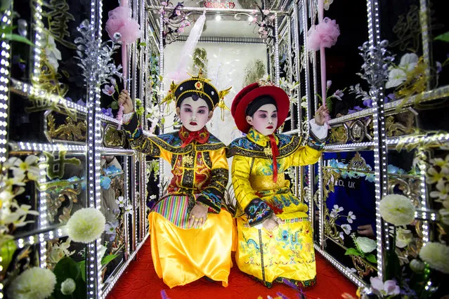 Young performers in costumes standing high on plank platforms and other people carrying poles below parade on the streets during folk dance “Taige” before the Lantern Festival on February 26, 2018 in Taizhou, Zhejiang Province of China. “Taige”, a folk dance that originated in Southern Song Dynasty, is always performed by teenagers dressed up as characters from historical stories or legends to wish for favorable weather and good harvest in fishing. (Photo by VCG/VCG via Getty Images)
